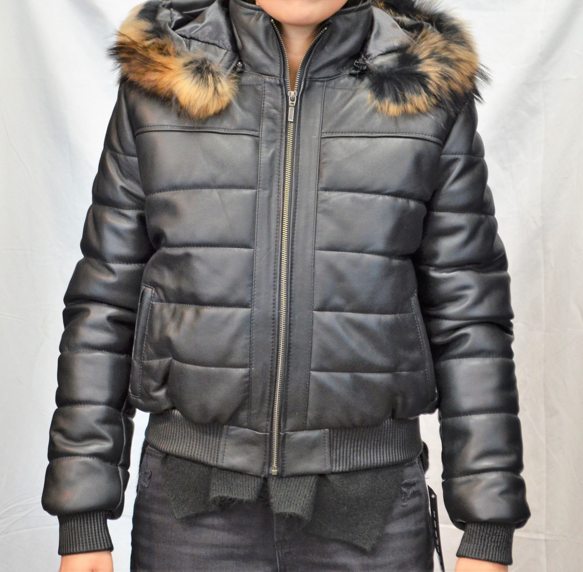 Front view of leather jacket on model with light puffer design and real fur hood, zipped up and hands to sides. 